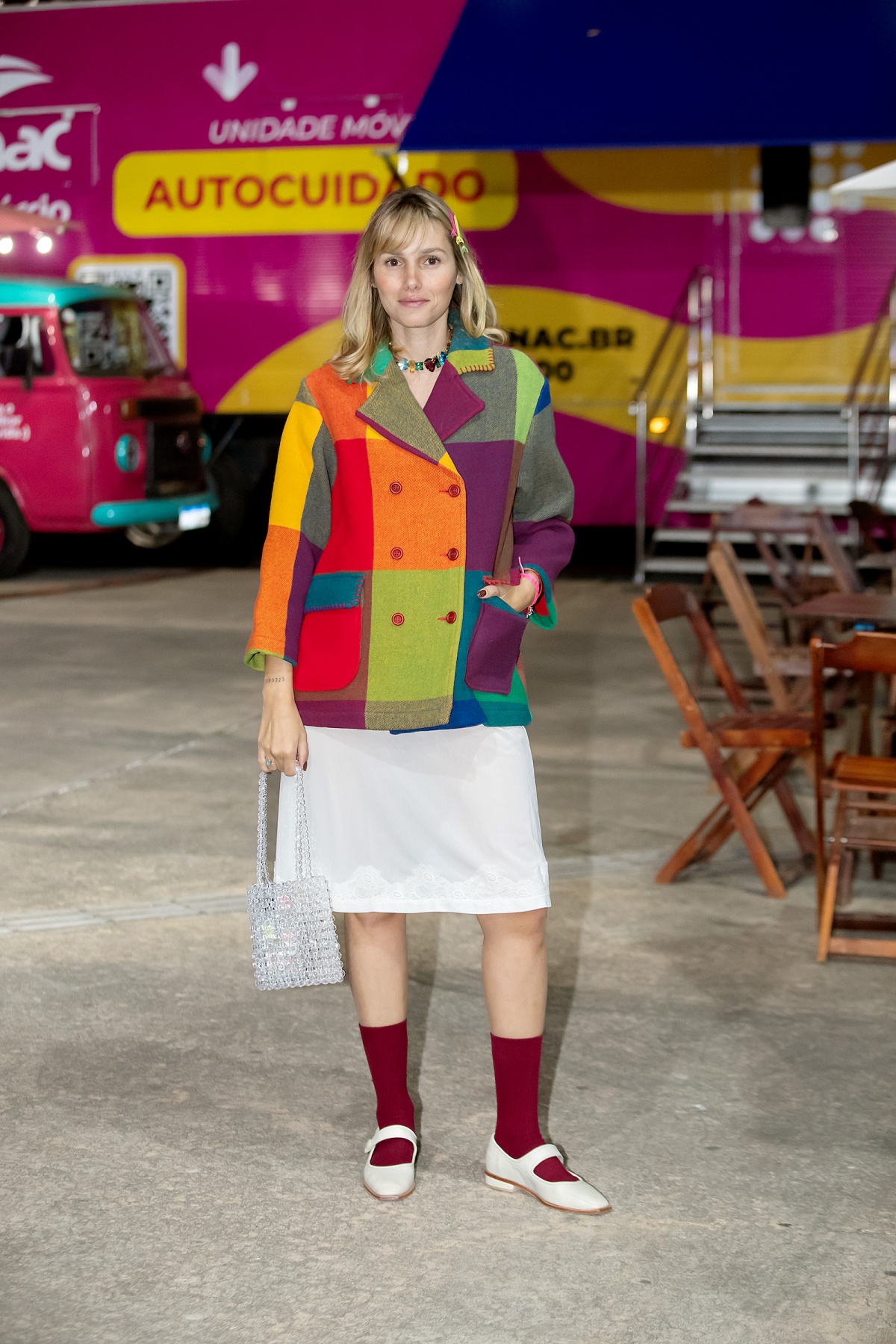A imagem mostra uma mulher de blazer xadrez colorido, saia branca, meia vermelha e sapatilha branca