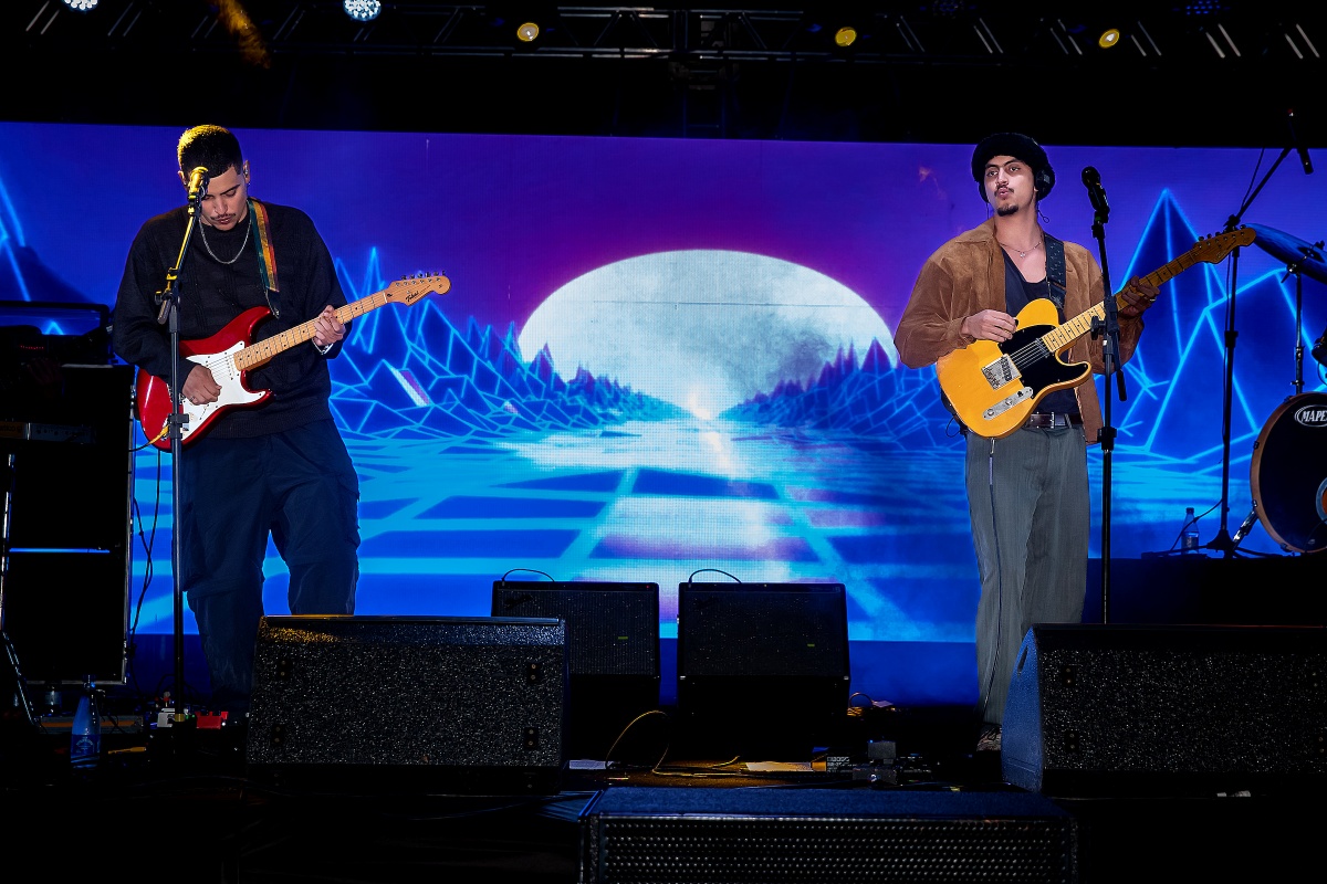 A imagem mostra dois artistas cantando em palco de evento