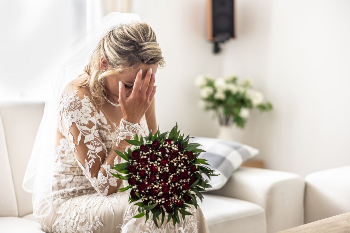 Foto colorida de mulher vestida de noiva com a cabeça baixa 