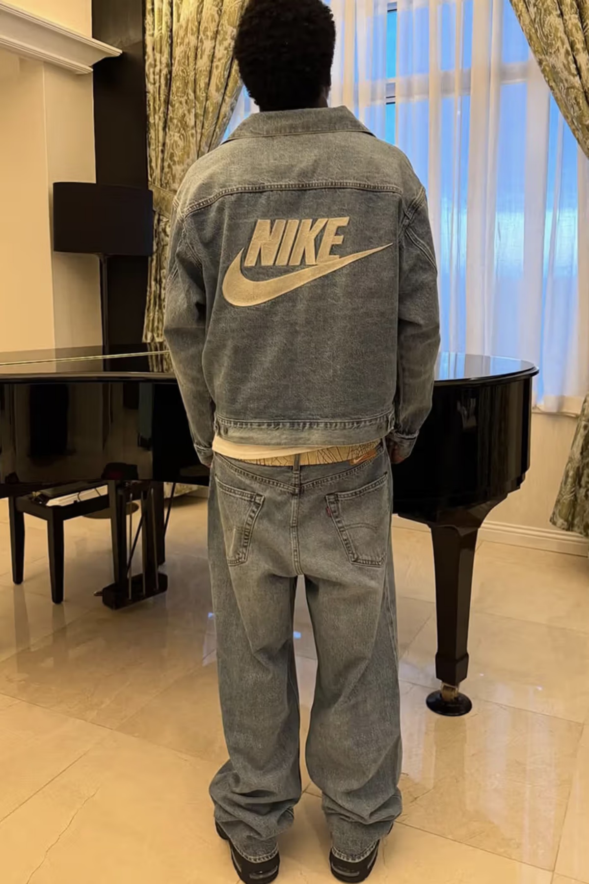 A imagem mostra um homem de costas vestindo um conjunto de jaqueta e calça jeans