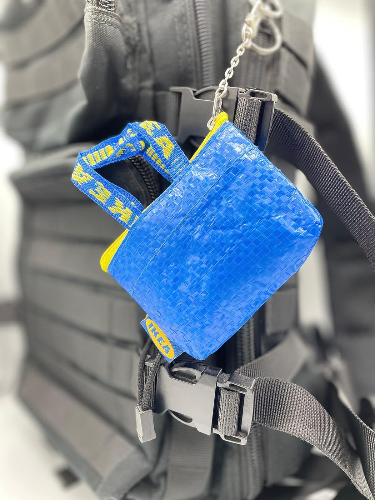 A imagem mostra uma mini bolsa azul com detalhes amarelos presa em uma bolsa preta