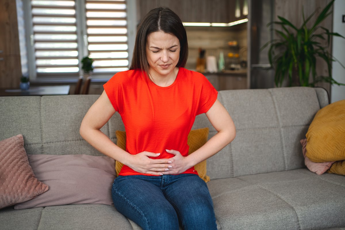 Mulher sentada em um sofá e com a mão na barriga - Metrpopoles