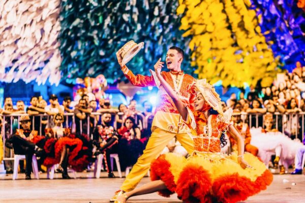 Foto colorida, de uma festa de junho, várias pessoas cantam e um casal de destaque - metrópole