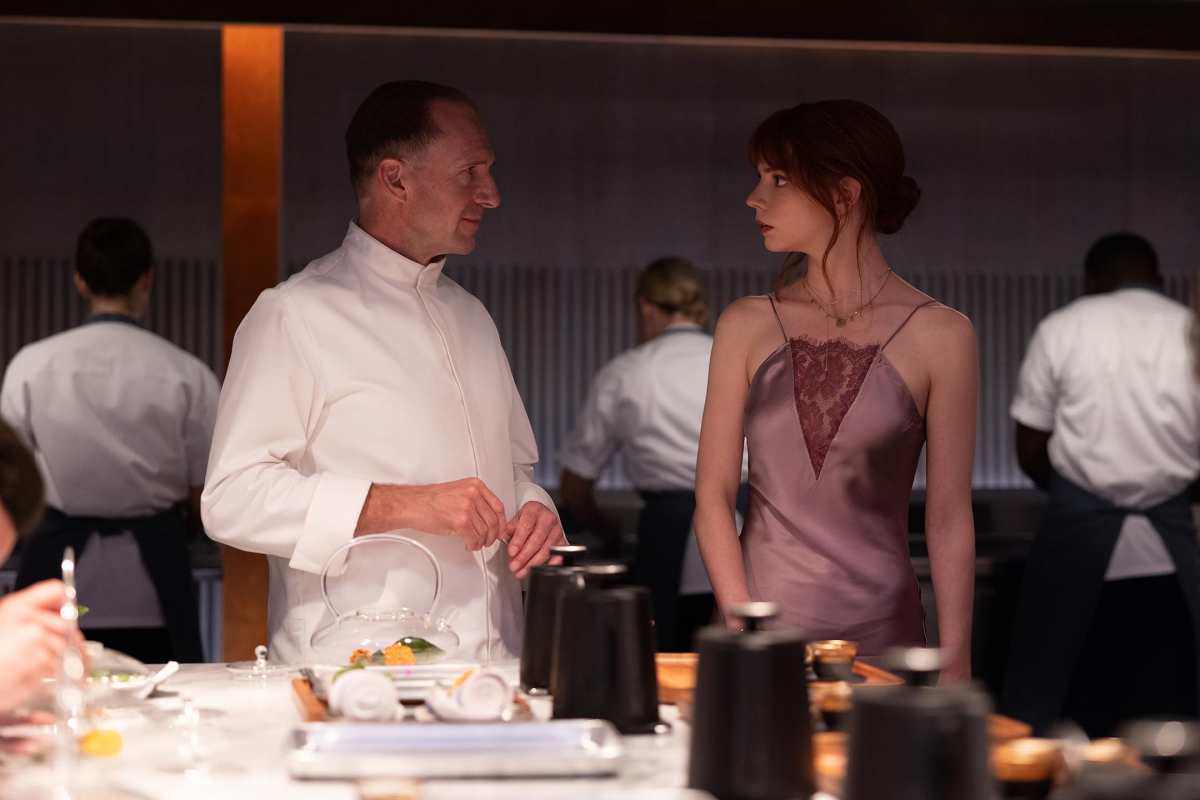 A imagem retirada do longa O Menu (2022) mostra um homem em pé ao lado de uma mulher
