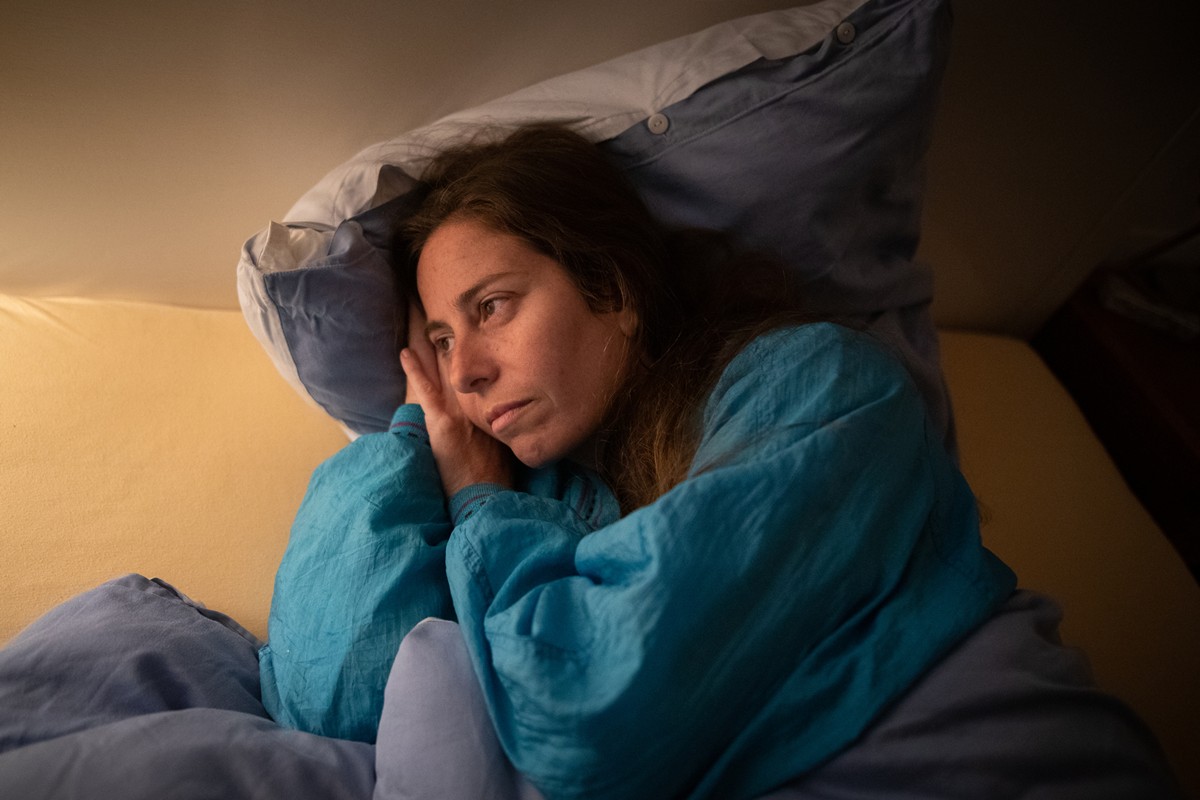Foto colorida de mulher deitada na cama. Ela está acordada - Metrópoles