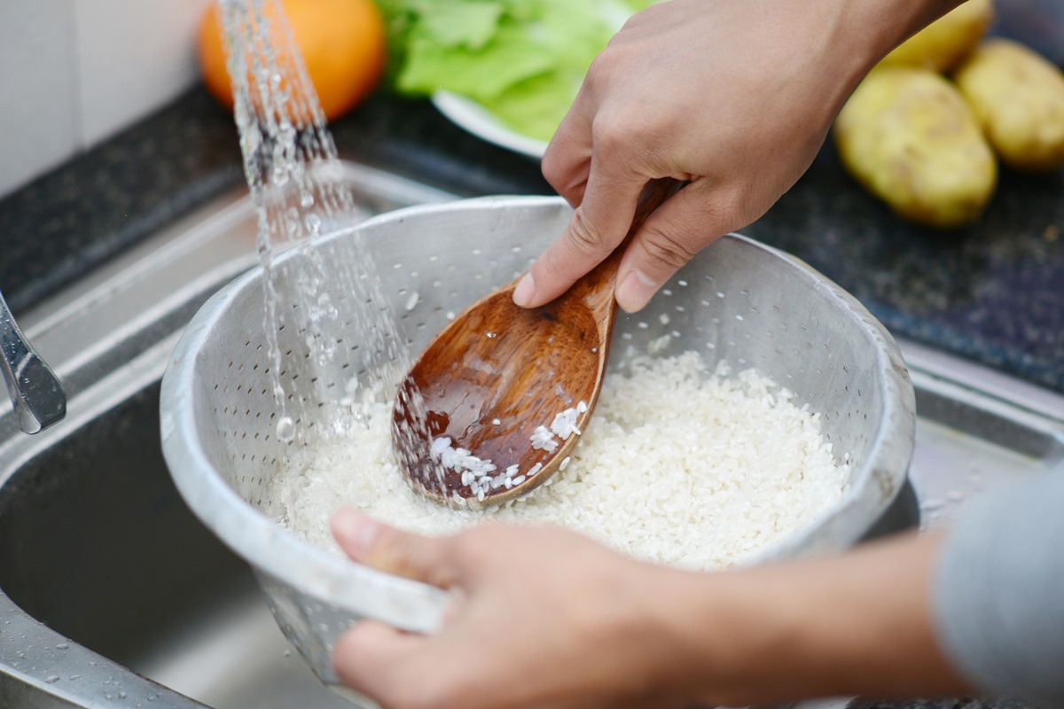 Foto em close up lavando arroz branco na pia. Metrópoles