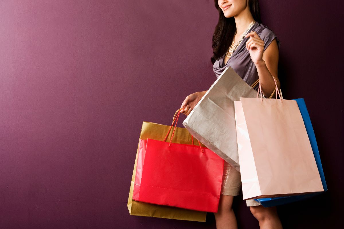 foto colorida de uma mulher com várias sacolas de compras 
