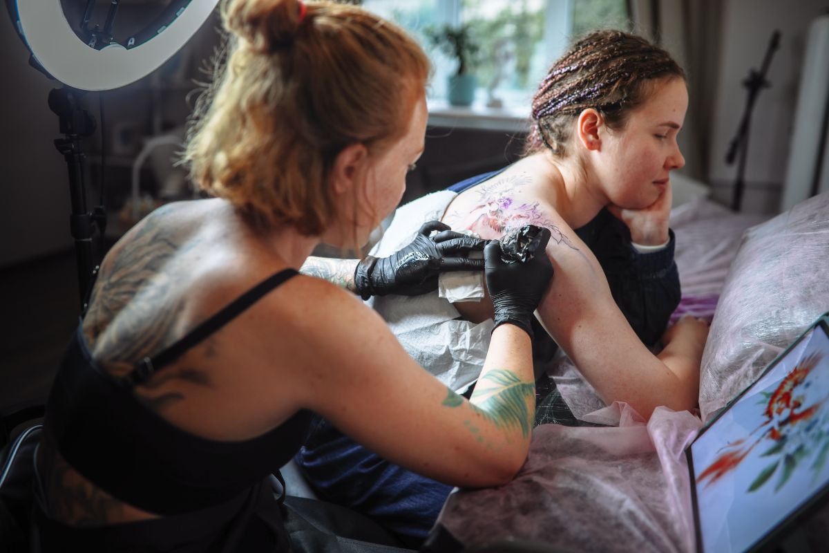 foto colorida de uma tatuadora tatuando outra mulher 