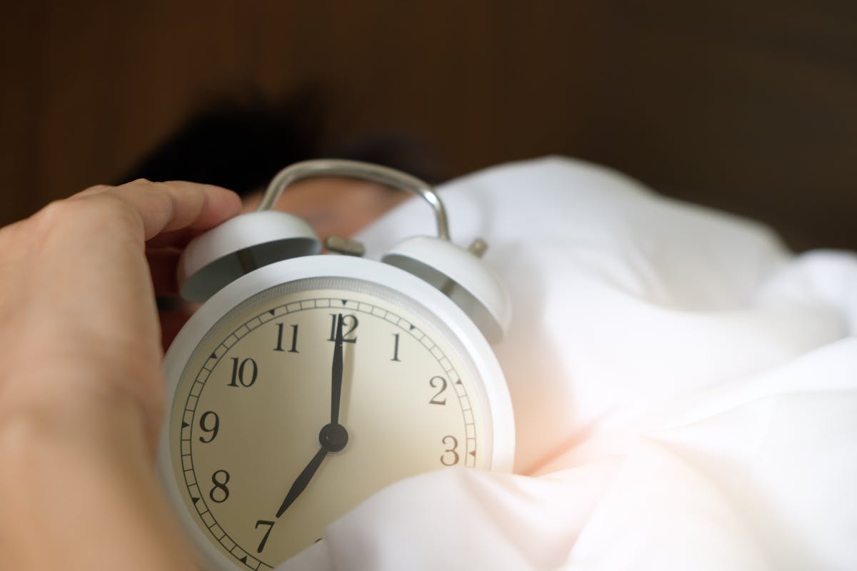 Mão segurando relógio em cima de cama - Metrópoles