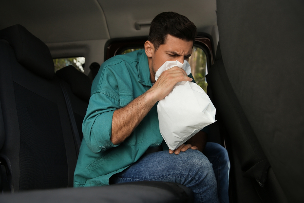 Homem branco segurando saco branco de enjoo em banco de trás de carro - Metrópoles
