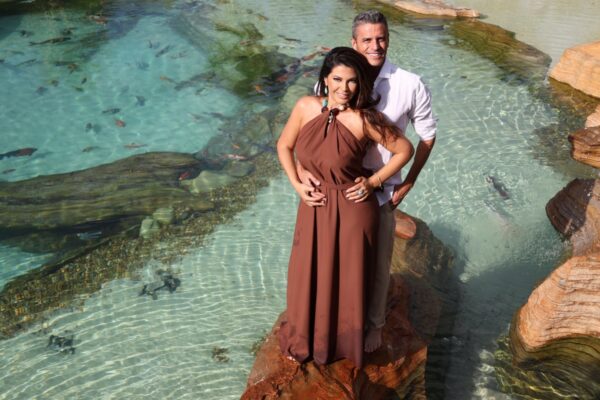 foto de um casal de meia idade bem joviais e saldáveis em meio a uma praia artificial de agua cristalina