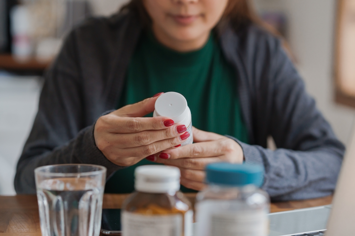 Mulher asiática lendo o rótulo de um medicamento ou suplemento alimentar - Metrópoles