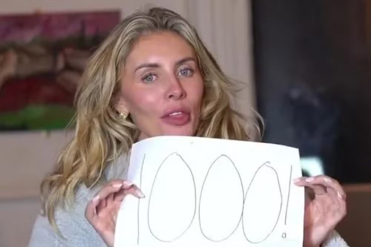 foto colorida de mulher loira segurando uma placa com o número 1000