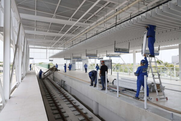 Estação de VLT coberta, moderna e ampla, com passageiros caminhando pela plataforma branca.