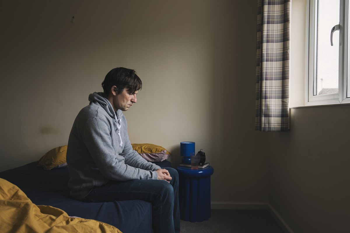 Foto de homem sentado na cama se sentindo sozinho, triste e depressivo. Lojas de conveniência, solidão