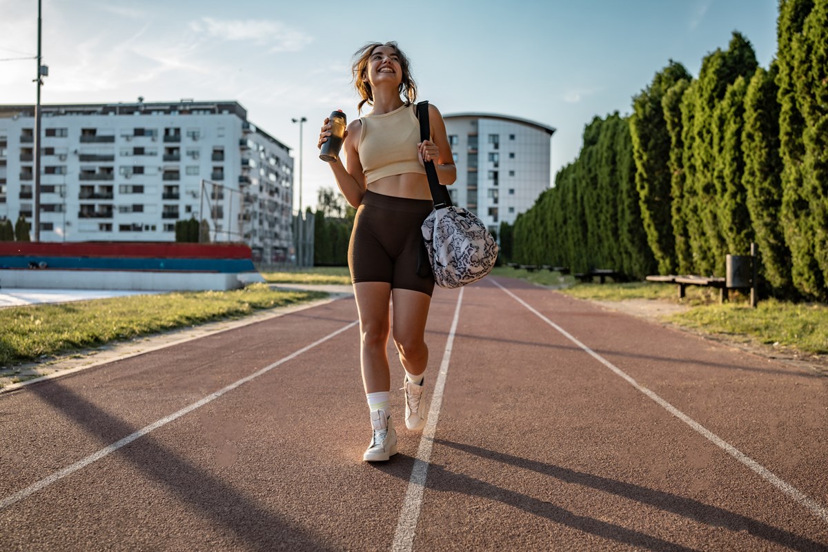 Foto colorida de mulher alegre caminhando em uma pista de corrida ao ar livre - Metrópoles