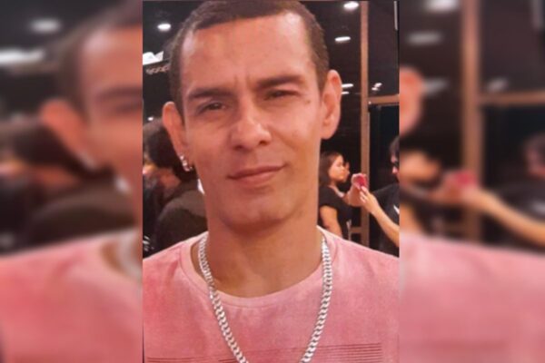 Foto colorida de homem magro com blusa rosa e cordão prateado