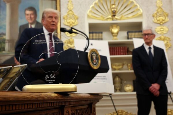 Foto colorida de Donald Trump discursando atrás de um disco de vidro, presenteado a ele pelo CEO da Apple, Tim Cook (à direita), durante um evento no Salão Oval da Casa Branca, em 6 de agosto de 2025, em Washington, D.C. - Metrópoles