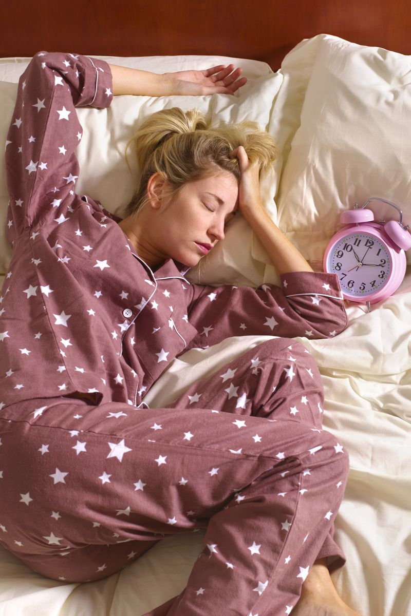 Foto colorida de mulher deitada em cama ao lado de um relógio - Metrópoles