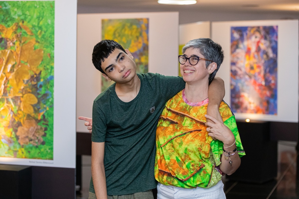 Imagem colorida de mãe e filho com autismo sindrômico durante exposição - Metrópoles