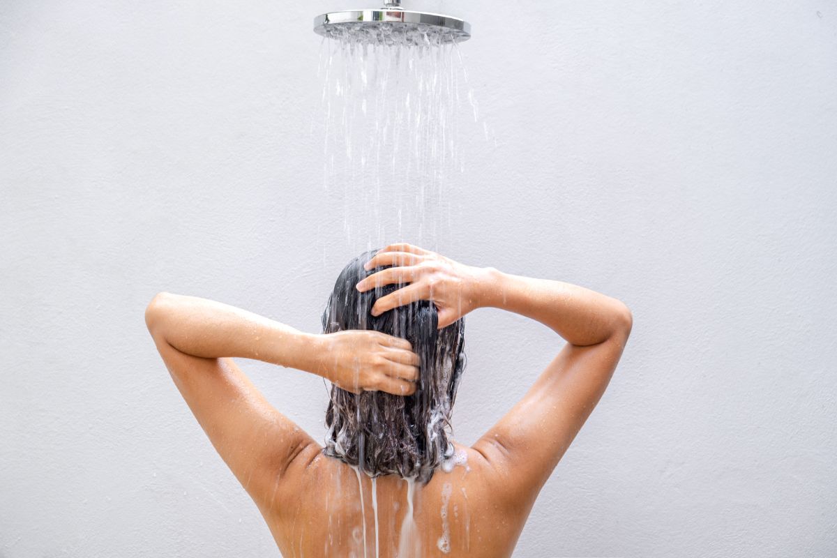 Mulher tomando banho no chuveiro, com espuma no cabelo