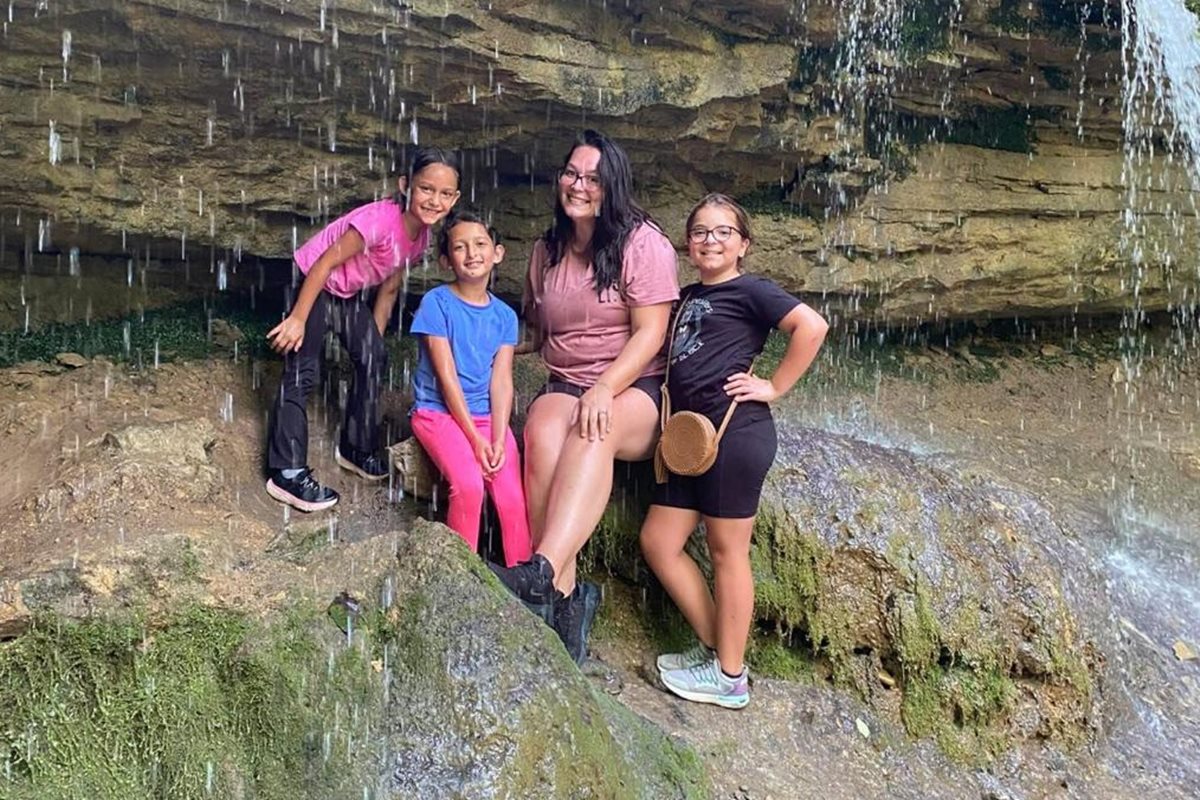 Foto colorida de uma mulher mais velha rodeada de três crianças durante uma trilha para a cachoeira - Metrópoles.