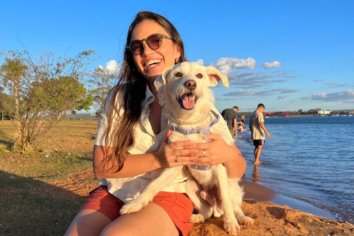 Imagem colorida de mulher abraçada com cachorro vira-lata branco