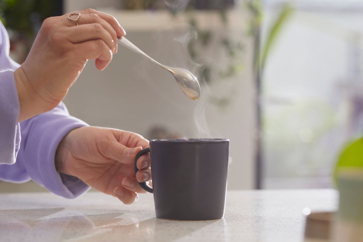 Mulher de blusa longa lilás misturando café em uma xícara preta quente