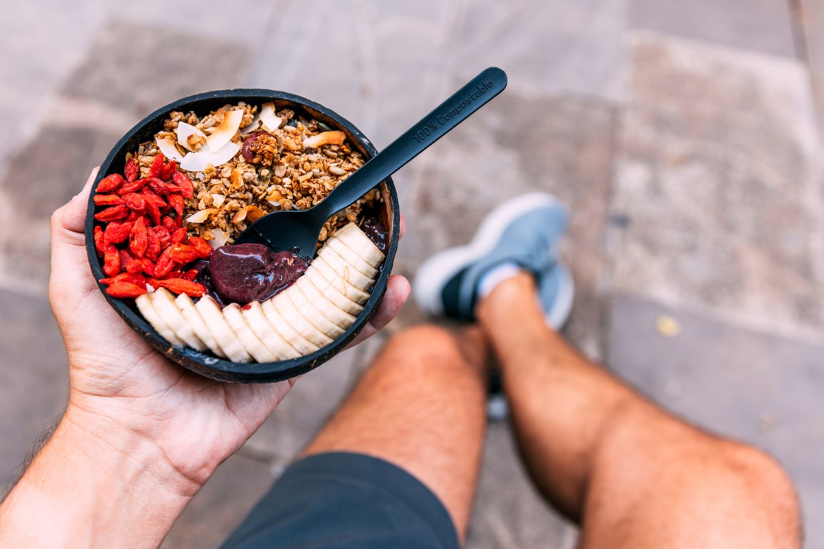 Foto colorida de bowl com frutas e oleaginosas segurado por uma mão masculina - Metrópoles