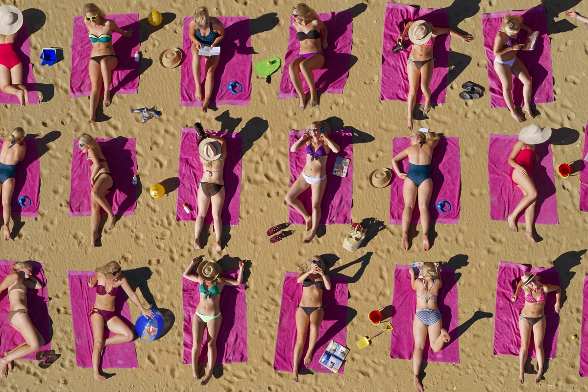 Foto colorida de pessoas pegando sol na praia - Bronzeamento natural: entenda riscos e cuidados da exposição ao sol