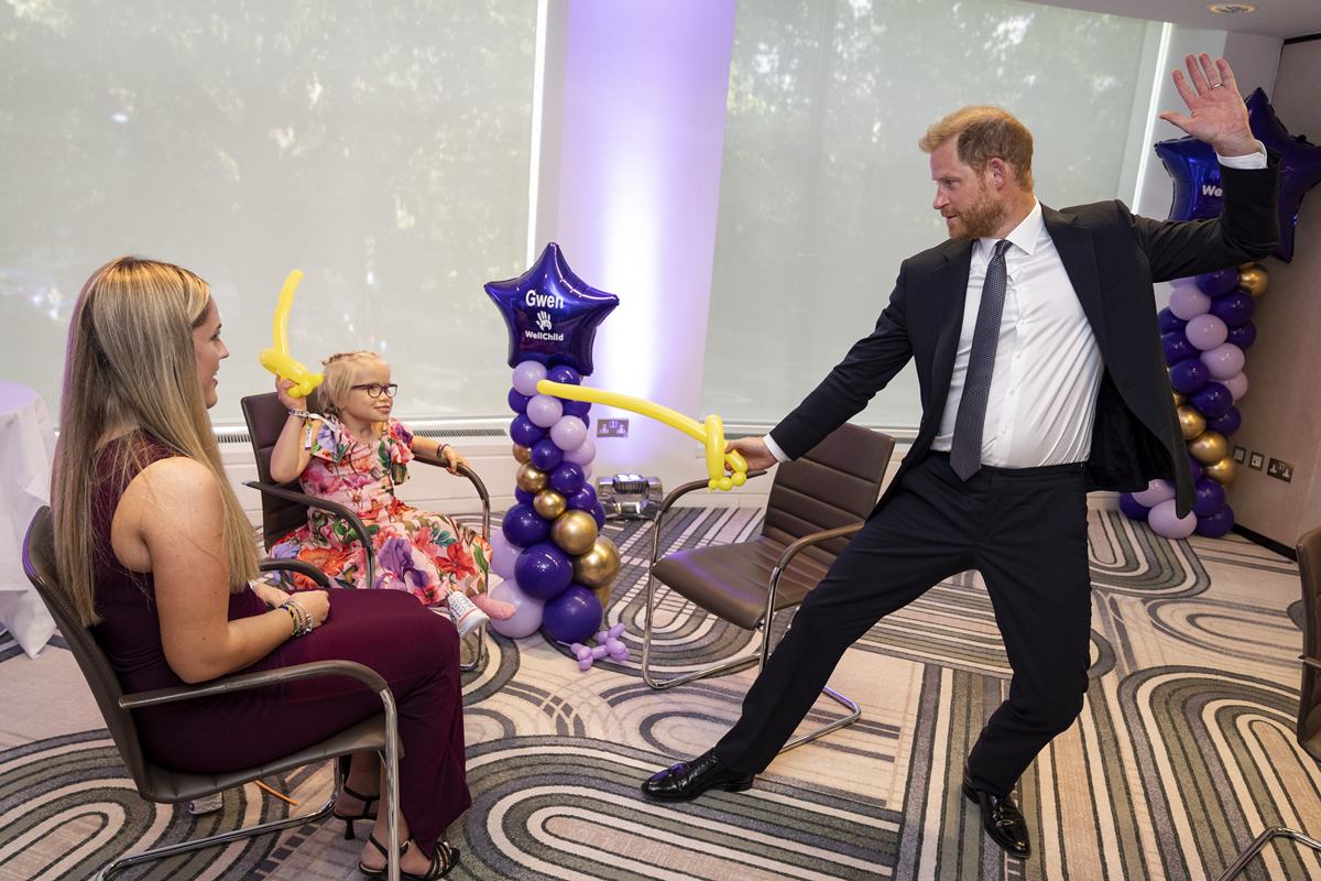 Foto colorida de homem segurando balão. Ele brinca com uma menina que está sentada - Metrópoles