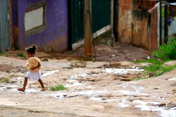 Menina criança, caminha com um urso na mão em chão de barro