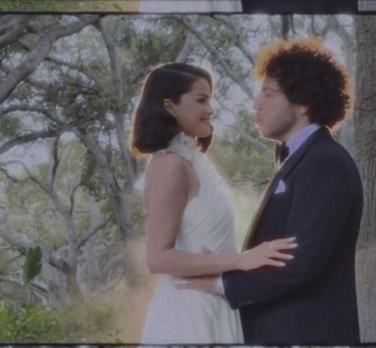 Imagem colorida de Selena Gomez em vestido de noiva abraçada com Benny Blanco