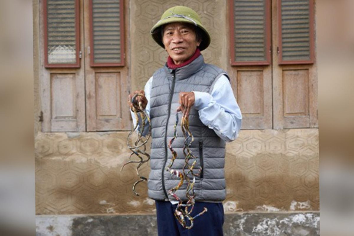 Foto colorida de homem asiático vestido com calça escura, blusa branca e colete cinza, chapéu e unhas inacreditavelmente grandes.