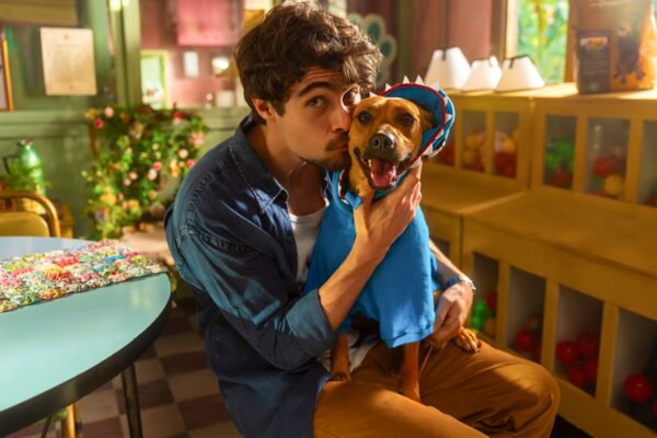 Imagem de Rafa Vitti caracterizado para o filme Caramelo ao lado de um cachorro sorrindo para a câmera