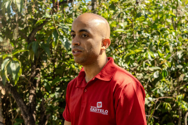 Homem de camisa vermelha com logotipo da Castelo Forte, fala em meio à vegetação