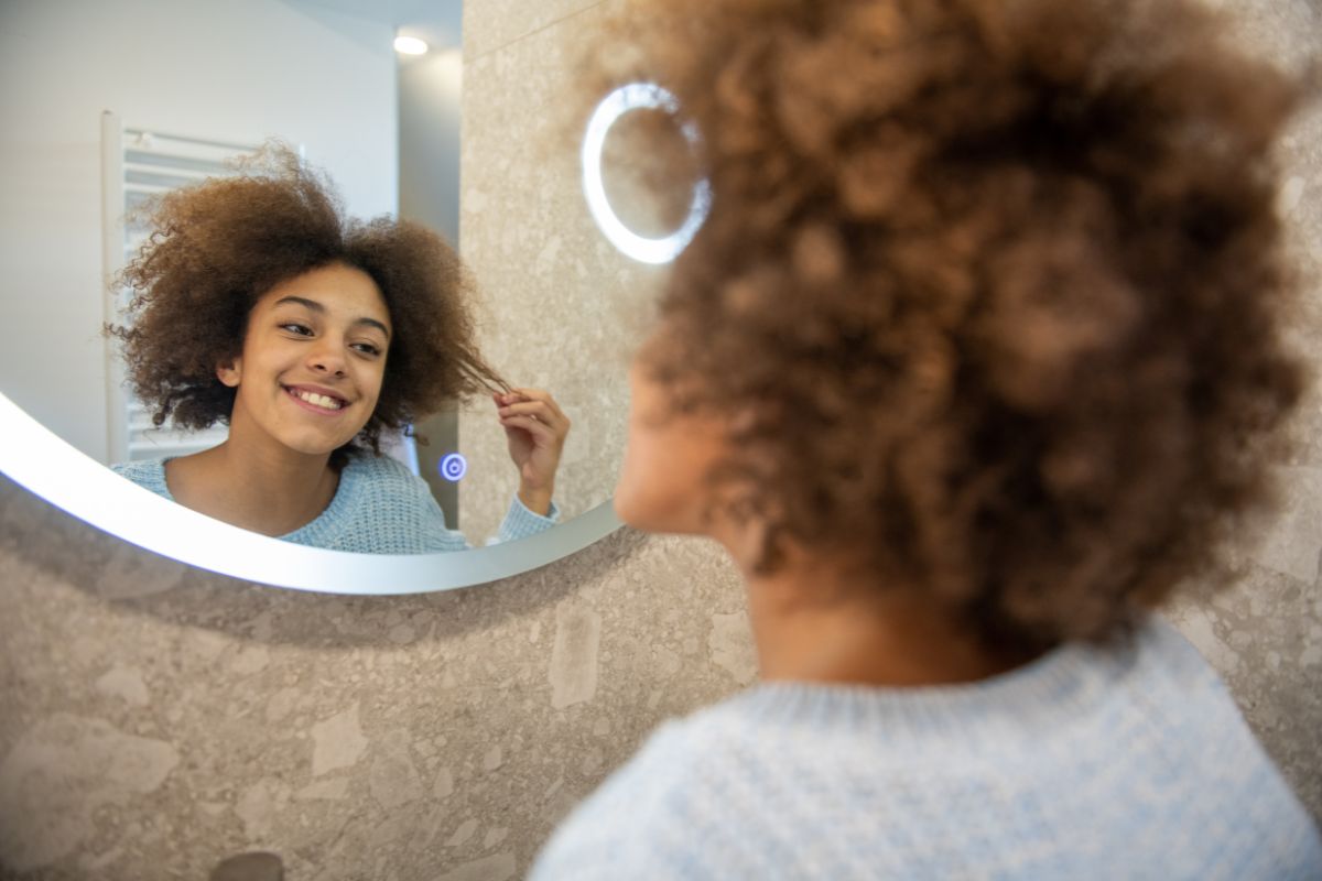 Foto colorida de uma menina penteando o cabelo - Metrópoles