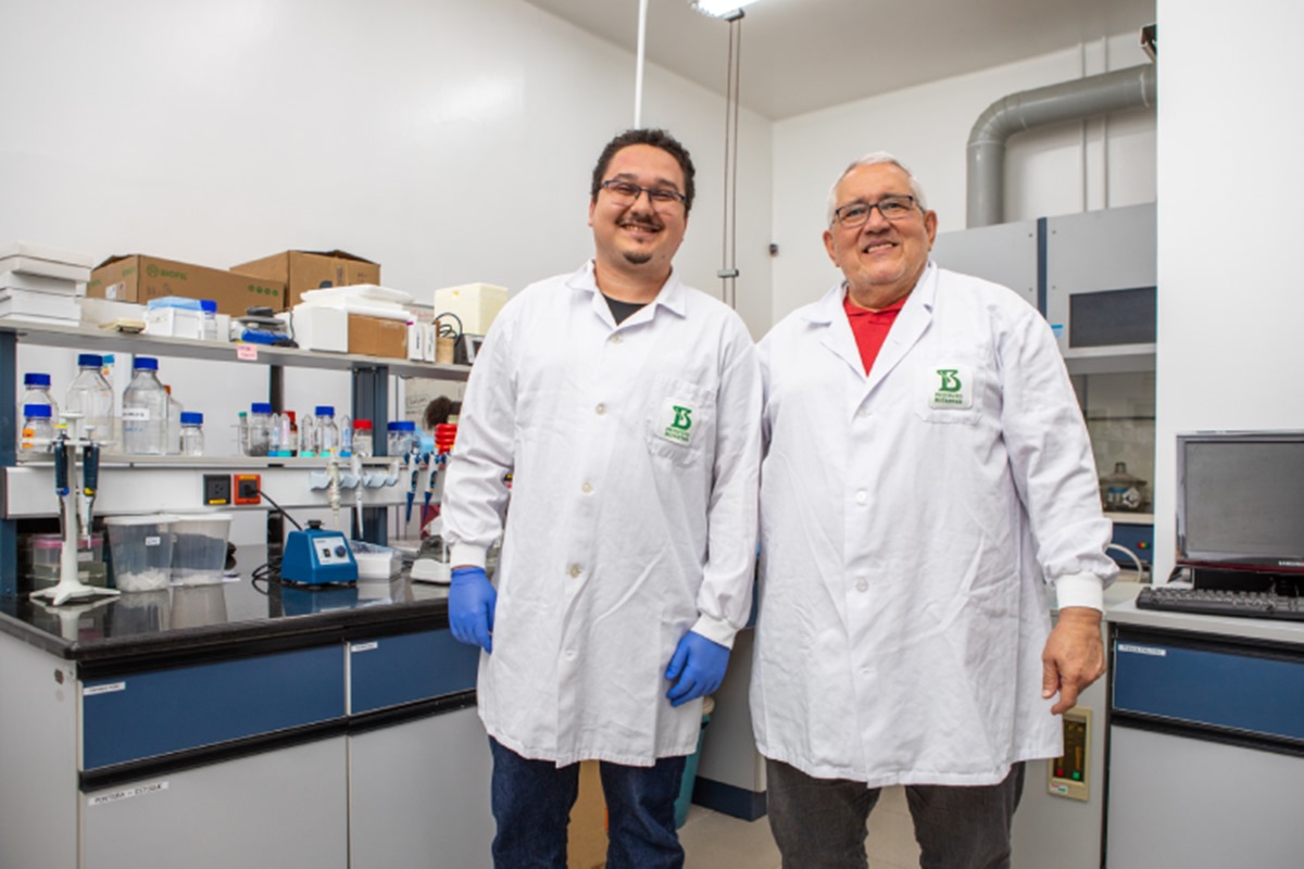 Imagem colorida mostra dois brancos com jaleco dentro de um laboratório sorrindo para foto - Metrópoles