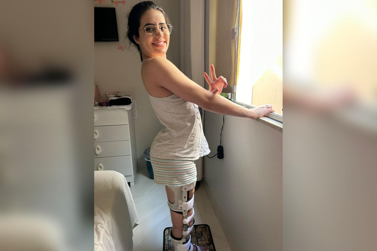 Foto colorida de mulher jovem usando uma espécie de prótese nas pernas enquanto sorri para foto. -Metrópoles.