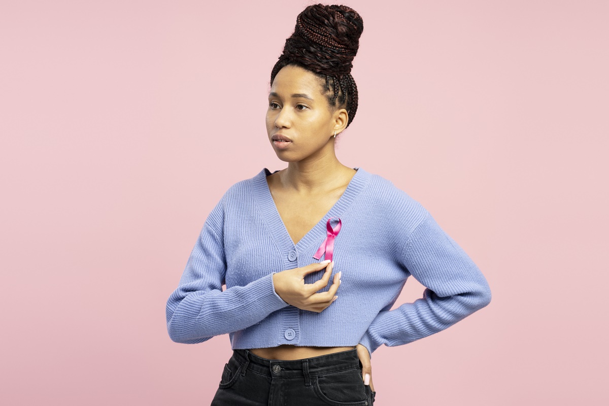 Foto colorida de mulher segurando o símbolo de combate ao câncer de mama - Desigualdade afeta tratamento de câncer de mama em mulheres negras - Metrópoles