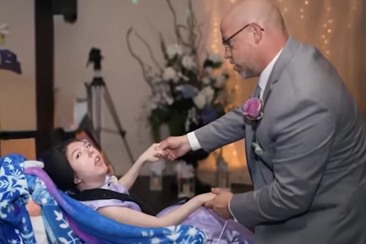 Foto colorida de homem segurando a mão de uma gartoa deficiente sentado em cadeira de rodas - Metrópoles. 