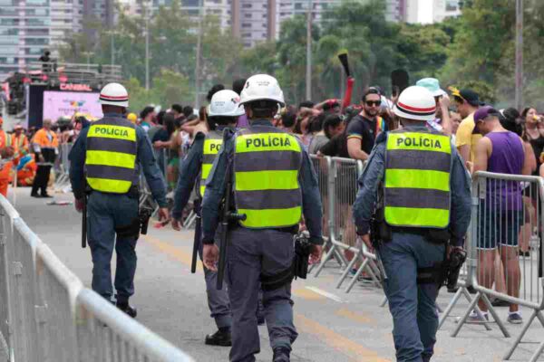 Homens da polícia militar andam de costas em meio a bloco de carnaval.